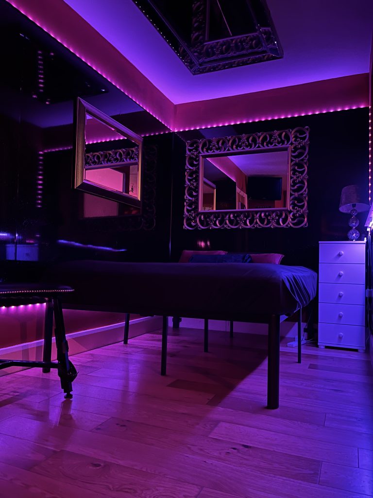 The same bedroom lit in purple and pink, with mirrored ceiling
