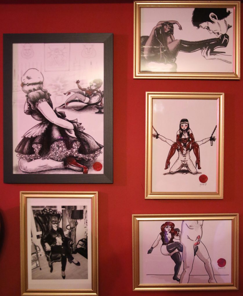 Framed black-and-white and colour fetish illustrations on the red dungeon wall
