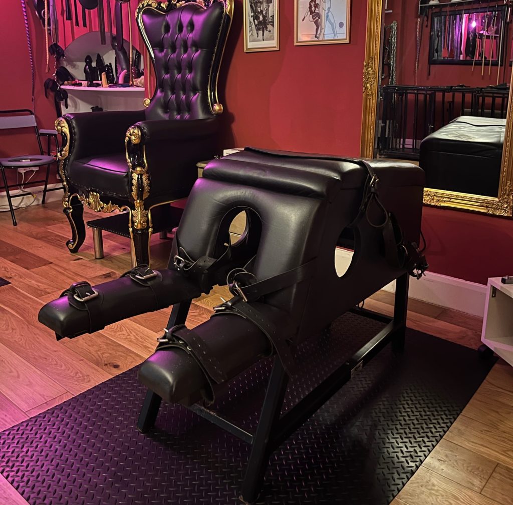 Padded leather spanking bench with restraints next to the black and gold throne
