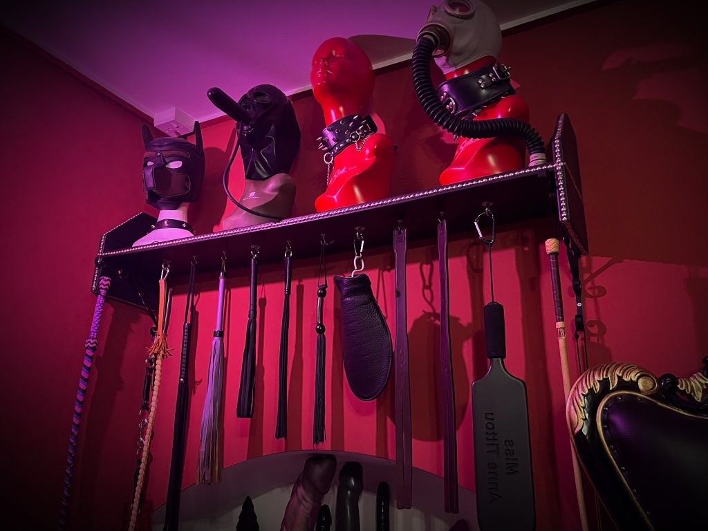 Rack of hoods and gas masks above canes, crops, floggers and paddles