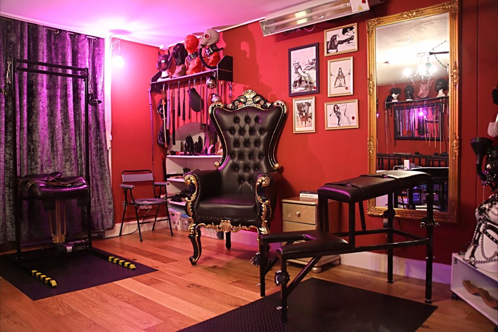 Main dungeon room with throne, spanking bench, wall of impact toys and purple velvet curtains