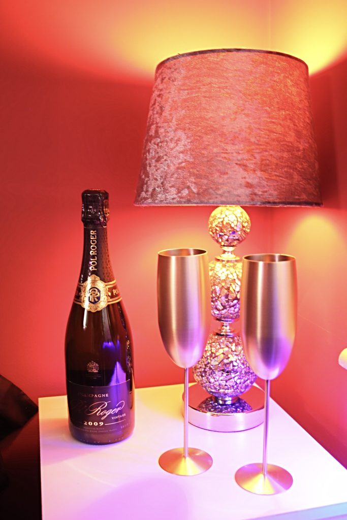 Champagne bottle and two gold flutes under a red glass lamp