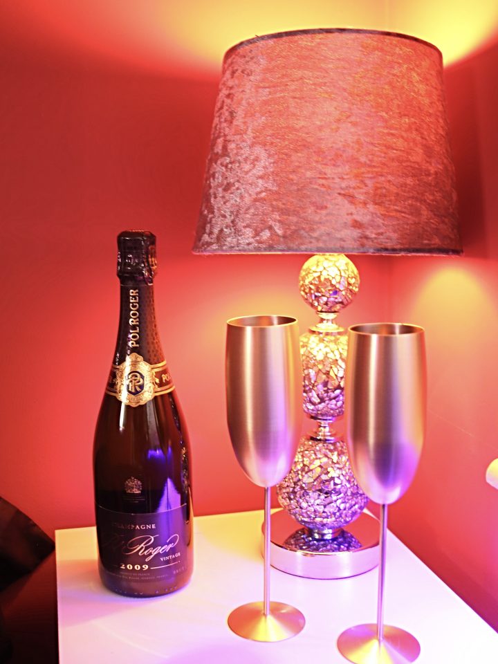 Champagne and gold flutes under a red lamp in the suite