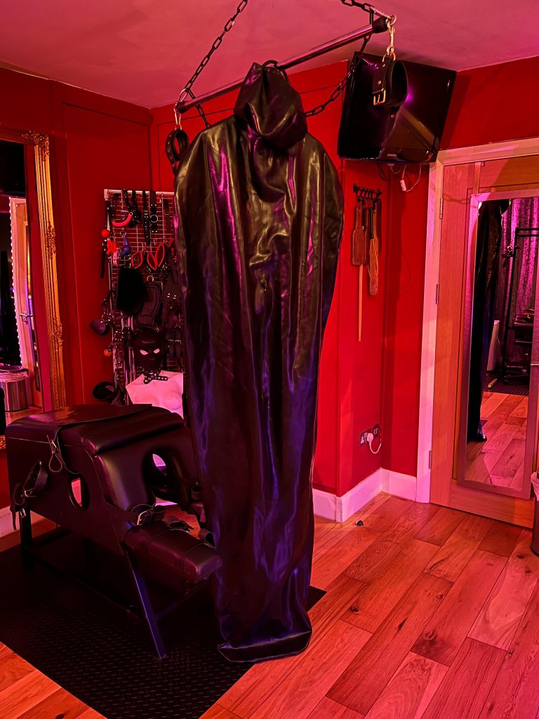 Black rubber body bag hanging from a ceiling hoist in the red dungeon