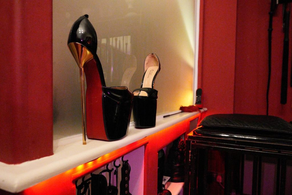 Black and nude platform stiletto heels on a red-lit shelf