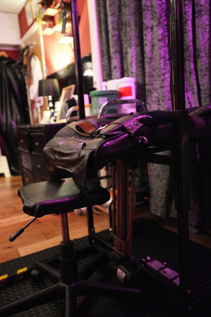 Adjustable stool and leather restraints by the purple velvet curtains