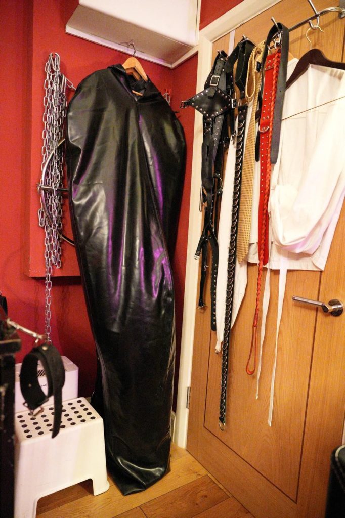 Rubber sleep sack hanging beside chains, collars and leads on the door