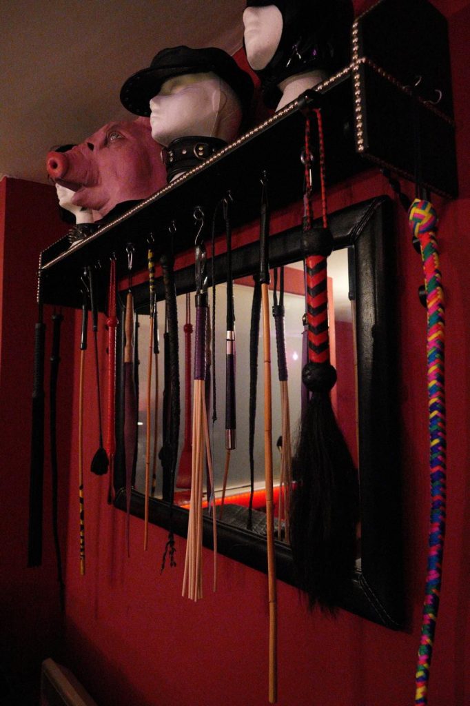 Rack of canes, whips and floggers below a shelf of hoods