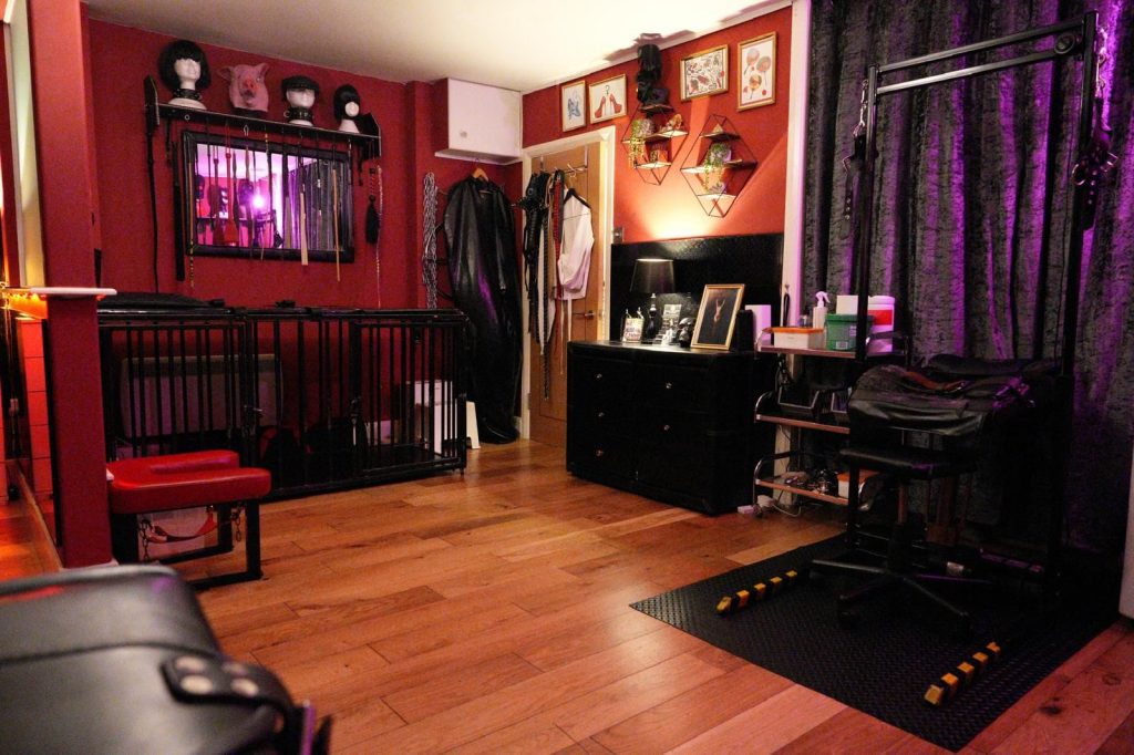 Red dungeon room with cage bed, black chest of drawers and purple velvet curtains