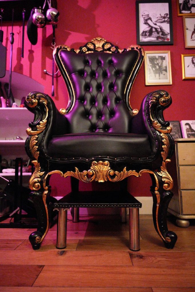 Black leather throne with carved gold frame and footstool on a red wall