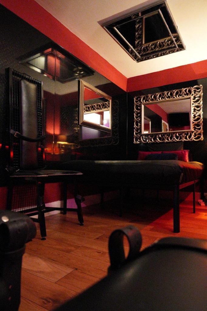 Dark bedroom with mirrored ceiling panel, ornate mirror and leather bench