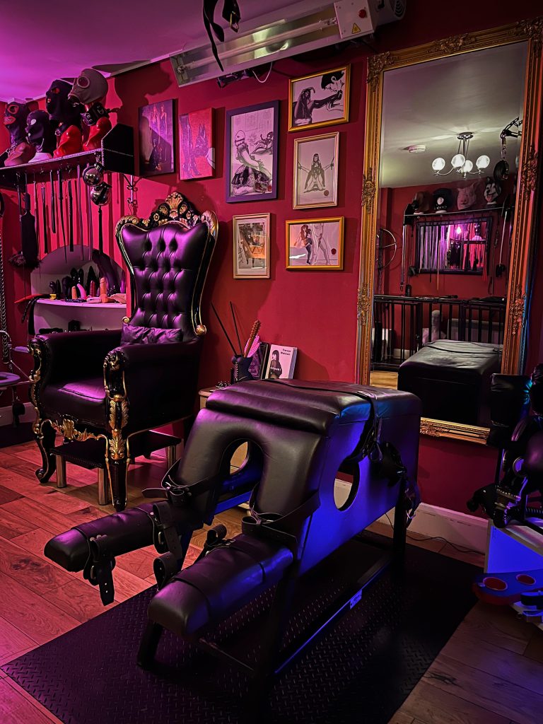 Padded spanking horse with leg rests, throne and gold mirror in the red dungeon