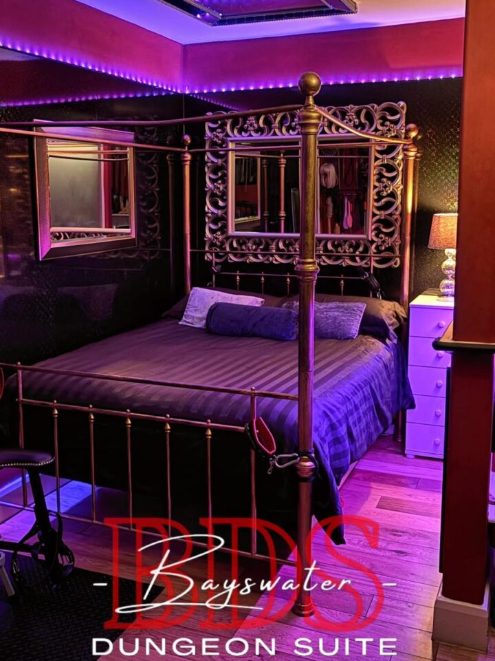 Brass four-poster bed with ornate gold mirrors and purple LED lighting in the overnight dungeon bedroom