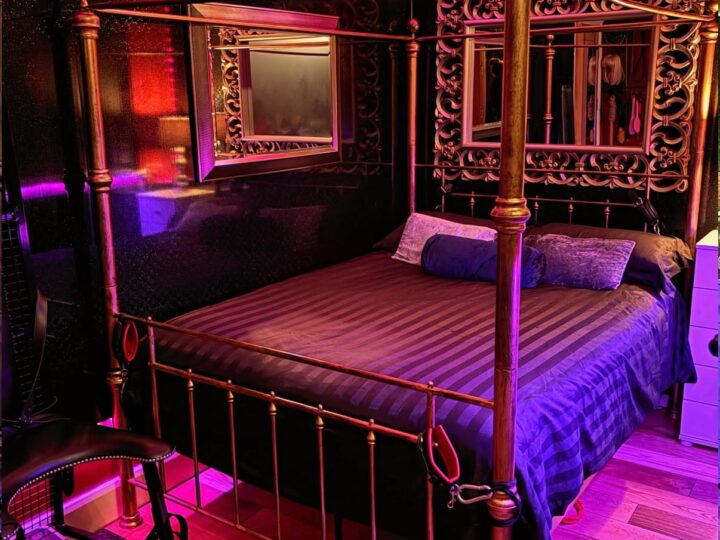 Four-poster bed under pink neon with ornate gold mirrors in the London BDSM hotel room